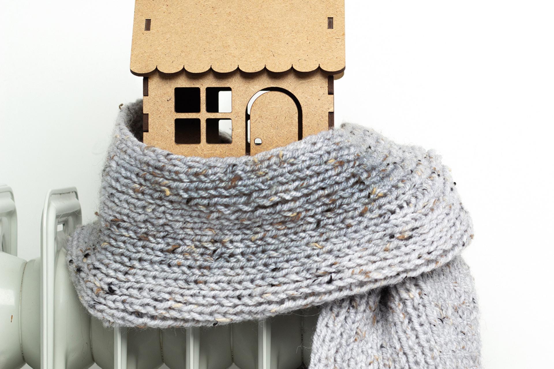 Foto van houten huisje in een sjaal gewikkeld, staand op de verwarming.